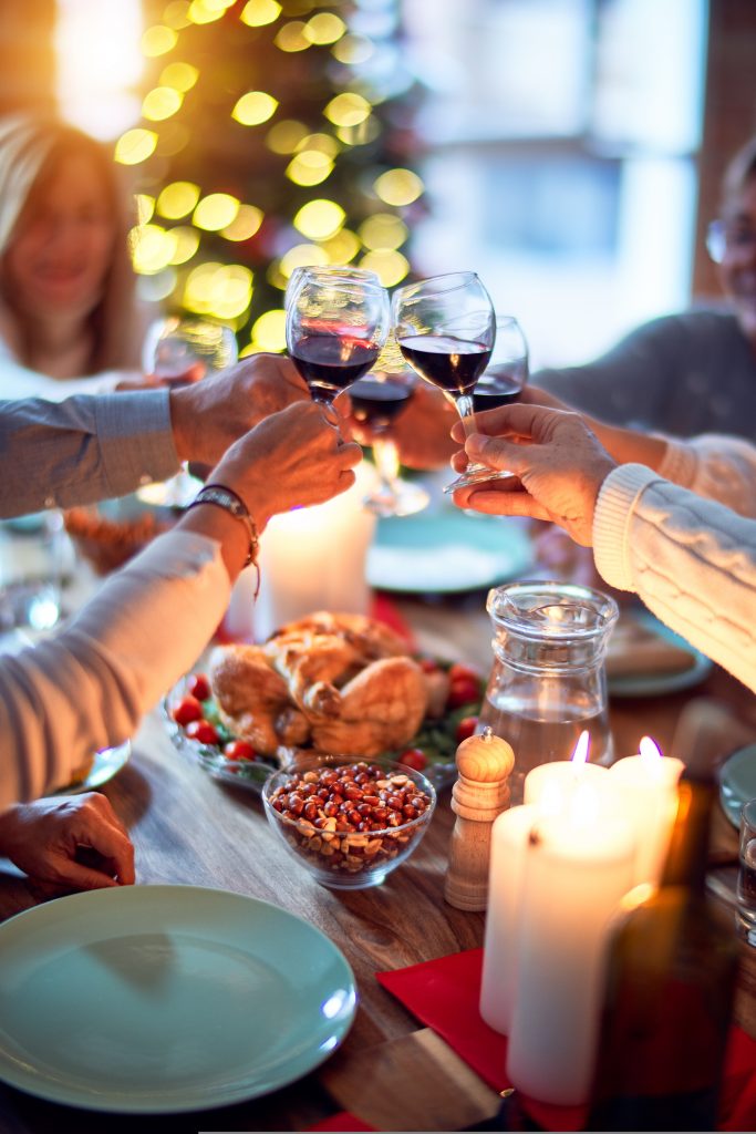 people cheersing glasses of red wine over a holiday dinner spread