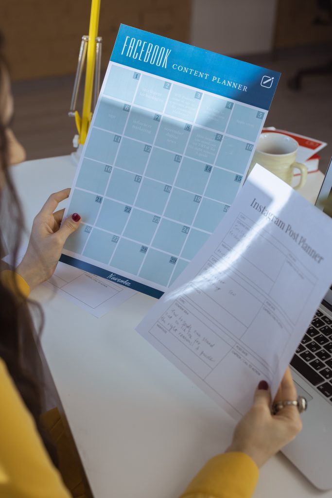 person holding a Facebook post planner document and an instagram post planner document
